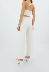 Top court smocké blanc avec un lien halter, associé à un pantalon large et des sandales à plateforme. Texture lisse et design minimaliste.