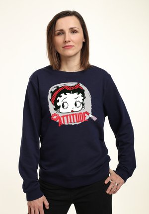 Marineblå sweatshirt med grafik af en tegneseriefigur med et rødt pandebånd. Teksten "ATTITUDE" står med fede røde bogstaver. Blød tekstur.