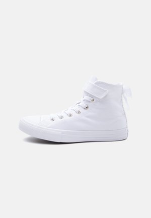 Hvite høye sneakers med lisser, en borrelåsstropp rundt ankelen, og en gummisåle, vist fra innsiden på en lys bakgrunn.