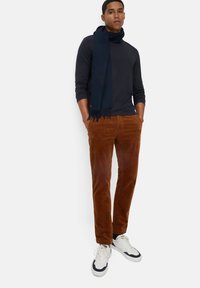 Marine sjaal, zwarte lange mouwen top, bruine corduroy broek, witte sneakers met zwarte accenten. Geweven stof, comfortabele pasvorm, functionele zakken.