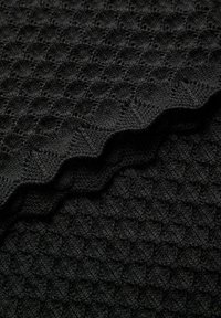 Tissu tricoté noir avec un motif losange texturé et des couches pliées montrant des coutures détaillées et un design tricoté en relief.