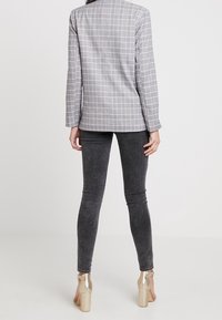 Šedý kostkovaný blazer s přiléhavým střihem, v kombinaci se tmavě šedými skinny džíny. Metalické zlaté boty na blokovém podpatku dodávají kontrastní prvek.