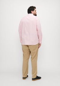 Camisa de manga larga rosa claro con cuello, detalle de yugo en la espalda, combinada con pantalones beige y zapatillas negras con suelas texturizadas.