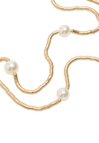 Naszyjnik z koralików w odcieniu złota, z naprzemiennie ułożonymi gładkimi perłami i teksturowanymi, cylindrycznymi koralikami, tworzącymi falisty, płynący wzór.