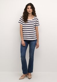 Haut à rayures à manches courtes en crème et bleu marine, col rond, coupe décontractée. Porté avec un jean bleu ajusté et des chaussures à talons beiges.
