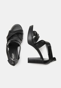 Sandali neri con tacco alto, caratterizzati da cinturini in pelle incrociati, chiusura con zip e un tacco a piattaforma texture. Finitura liscia in tutto il modello.