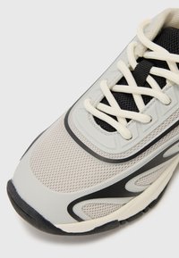 Baskets de sport grises avec empeigne en maille, accents noirs, lacets contrastés et semelle en caoutchouc. Présente un design texturé et un bout arrondi.