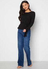 Top lungo a maniche ripiegate nero con cintura in vita, abbinato a jeans blu a vita media. Il tessuto testurizzato aggiunge una dimensione all'outfit.