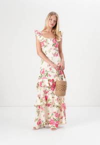 Blommig maxiklänning med volangärmar, med en krämvit bakgrund och rosa blommor. Burit med en vävd korgväska och platta sandaler.