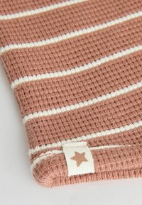 Rosa och vit randig tyg med en texturerad yta och en liten etikett med en stjärna. Mjukt, vävt och lätt material.