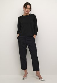 Pull en tricot noir avec un col rond et des détails en argent, associé à un pantalon sombre cintré et des escarpins argentés à bout pointu.