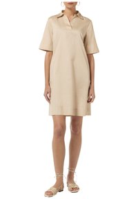 Vestido beige de cuello con mangas cortas hecho de una tela suave. Presenta un corte holgado, diseño hasta la rodilla y un escote en forma de V sutil. Combinado con sandalias de tiras.