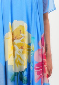 Floral dress in light blue sheer fabric, featuring large yellow and pink flower patterns, with short sleeves and a flowy design.