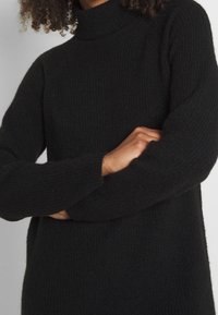 Pull ras du cou noir à côtes, avec des manches longues, fabriqué en mélange de laine texturé. Présente une coupe décontractée et une finition cosy.