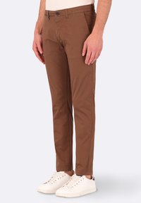 Chinos marroni in cotone con design slim fit. Presentano una chiusura con un solo bottone e tasche laterali. Abbinati a sneakers bianche.