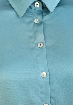 Light blue blouse featuring a collared neckline, textured fabric, and six pearl-like buttons along the front placket.