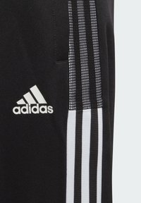 Pantalones deportivos negros con un tejido texturizado, acentos en blanco con tres rayas y un logo de Adidas bordado en blanco. Incluye un bolsillo lateral.