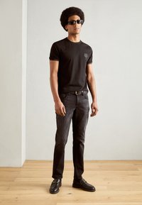 Zwarte katoenen t-shirt met korte mouwen en een klein logo, gecombineerd met donkere jeans en loafers. Gladde textuur en aansluitend ontwerp.