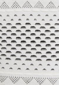 Un motif textile présentant des formes noires et blanches alternées, y compris des formes arrondies et des triangles, sur un fond de tissu clair.