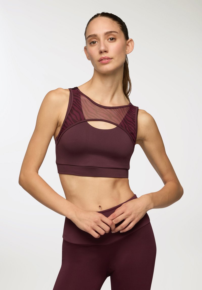 Bordowy stanik sportowy z siateczkowym panelem i wycięciem, o dopasowanym fasonie i gładkiej fakturze, w zestawie z pasującymi legginsami.