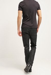 Jeans negros de mezclilla con corte ajustado, con bolsillos traseros y textura suave. Combinados con una camiseta negra ajustada y zapatos negros.