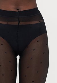 Schwarze, durchsichtige Strumpfhosen mit einem Polka-Dot-Muster, ausgestattet mit einem soliden Taillenbund und einer glatten Textur, die ein halbtransparentes Design hervorhebt.