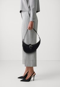 Borsa nera in finta pelle di coccodrillo con forma curvata, hardware argento e manico corto; abbinata a un completo a quadri bianco e nero e tacchi a spillo.