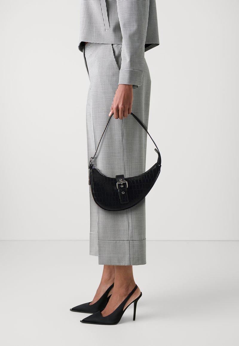 Borsa nera in finta pelle di coccodrillo con forma curvata, hardware argento e manico corto; abbinata a un completo a quadri bianco e nero e tacchi a spillo.
