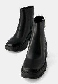 Bottines noires en cuir lisse avec une semelle épaisse, une fermeture éclair latérale et un bout arrondi. Design minimaliste sans motifs visibles.
