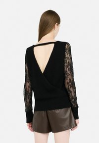 Maglione nero con profondo scollo a V sul retro; maniche lunghe in pizzo; corpo in maglia a trama. Abbinato a pantaloni corti in pelle marrone. Silhouette ordinata, linee pulite.