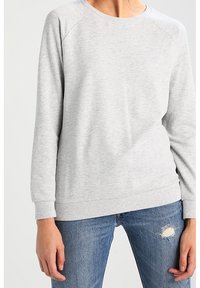 Felpa grigia chiara con collo a giro, maniche raglan e polsini e orlo a costine. Indossata sopra jeans blu con effetto usurato, tessuto testurizzato.