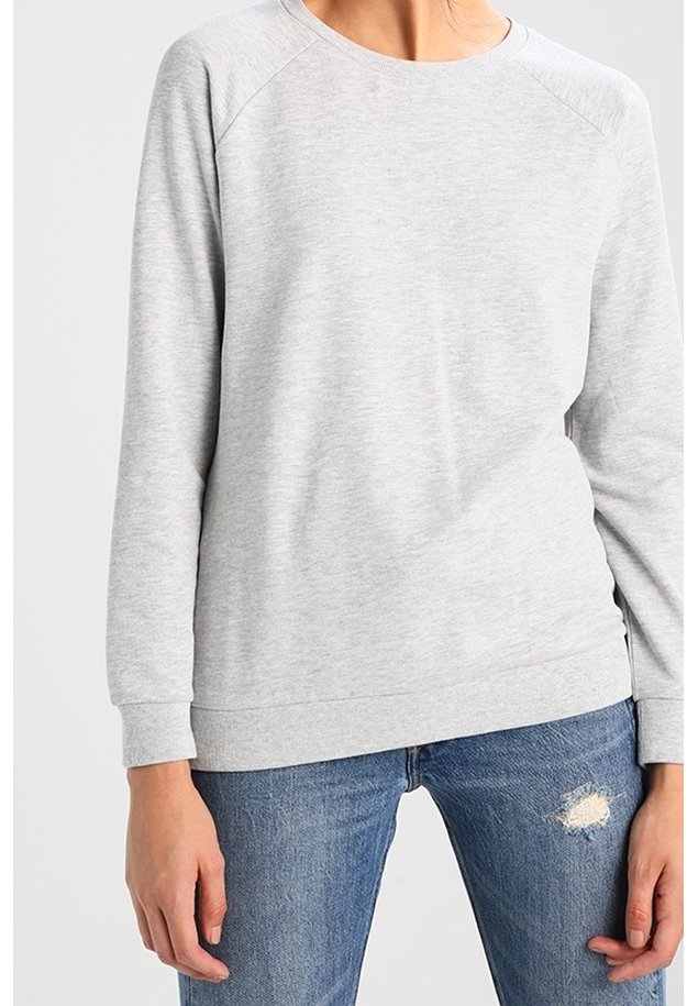 Felpa grigia chiara con collo a giro, maniche raglan e polsini e orlo a costine. Indossata sopra jeans blu con effetto usurato, tessuto testurizzato.