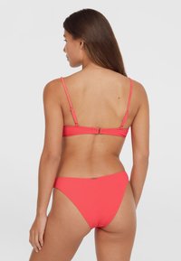 Pink ribbed bikini top with thin adjustable straps and clasps, paired with matching high-waisted bottoms. Smooth texture and simple design.