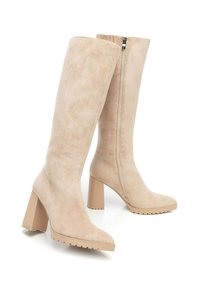 Beżowe zamszowe kozaki do kolan z szerokim obcasem, bocznym zamkiem, okrągłym noskiem oraz teksturowaną gumową podeszwą zapewniającą przyczepność.