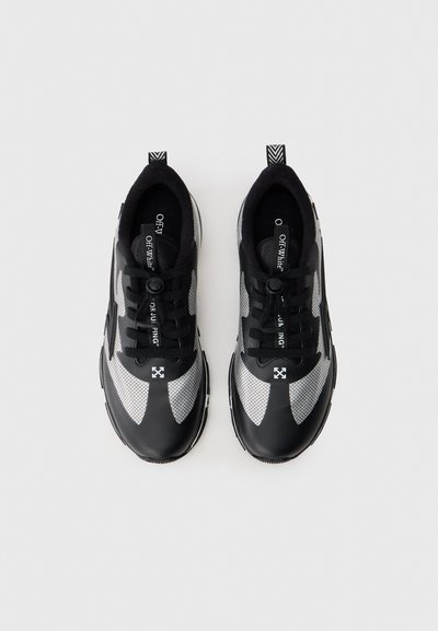 Μαύρα και γκρι αθλητικά παπούτσια με διχτυωτό επάνω μέρος και λείο λαστιχένιο δάχτυλο. Διαθέτουν κορδόνια και καλουπωμένο κουμπί. Διακοσμημένα με λεπτομέρειες λογότυπου και σχεδιασμό με σχέδια.