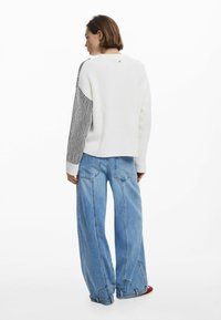 Gebreide trui met een witte body en zwarte gestreepte mouwen; gedragen met lichtblauwe wijde jeans; gestructureerde stof; casual pasvorm.