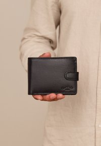 Černá kožená peněženka s hladkým povrchem, sklopným designem a zapínáním na knoflík. Vytlačené logo na přední straně.