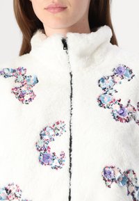 Weißer, kuscheliger Reißverschlussjacke mit hohem Kragen, verziert mit floralen Applikationen in Pastellfarben und metallischen Akzenten an den Seiten.