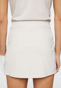 Beige golfhame, jolla on sileä pinta ja tiukasti istuva vyötärö. Takana pieni brodeerattu logo ja suora helma.