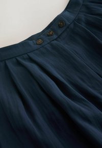 Marineblauwe geplooide rok van een gestructureerde stof, met drie bruine knopen in de taille en verticale lijnen voor extra detail.