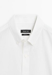 Hvid bomulds skjorte med knapper og klassisk krave, der har to frontknapper og en subtil tekstur. Etiketten siger "Massimo Dutti."