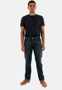 Donkerblauwe jeans met een slim fit, gecombineerd met een zwart t-shirt met korte mouwen. Schoenen zijn casual tan schoenen met een gladde textuur.
