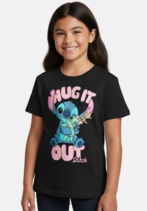 Lächendes Mädchen, das ein schwarzes T-Shirt mit dem blauen Cartoon-Charakter Stitch trägt, der eine Puppe umarmt, sowie rosa Text „Hug it out“ auf der Vorderseite.