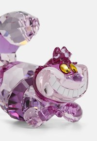 Klar kristallfigur av en grinande katt i nyanser av lila, med gula ögon, varierande fasetterade texturer och en stiliserad, krullad svans.