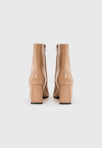 Botines de charol beige con tacón cuadrado, cremalleras laterales y textura lisa y brillante. Diseño sencillo, con detalles mínimos.