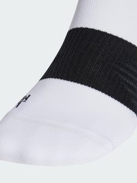 Chaussette de sport blanche avec une bande noire au niveau du mollet. Fabriquée en tissu texturé, avec un renforcement à la pointe et un accent de logo.