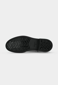 Semelle de chaussure noire avec des motifs de crampons profonds et le nom de la marque "GANT" avec la taille "42" embossé au centre.