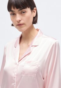 Ροζ σατέν πουκάμισο πιτζάμα με γιακά, κουμπιά μπροστά και μία τσέπη στο στήθος. Μαλακή υφή και άνετη εφαρμογή με μακριά μανίκια.