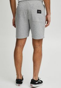 Lysgrå bomulds shorts med en afslappet pasform, der har en baglomme og et mærket patch. Sammen med sorte sneakers med lav snit.