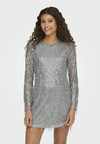 Vestido plateado con lentejuelas, de mangas largas y detalle de flecos. La tela es brillante y ajustada, mostrando una silueta recta.